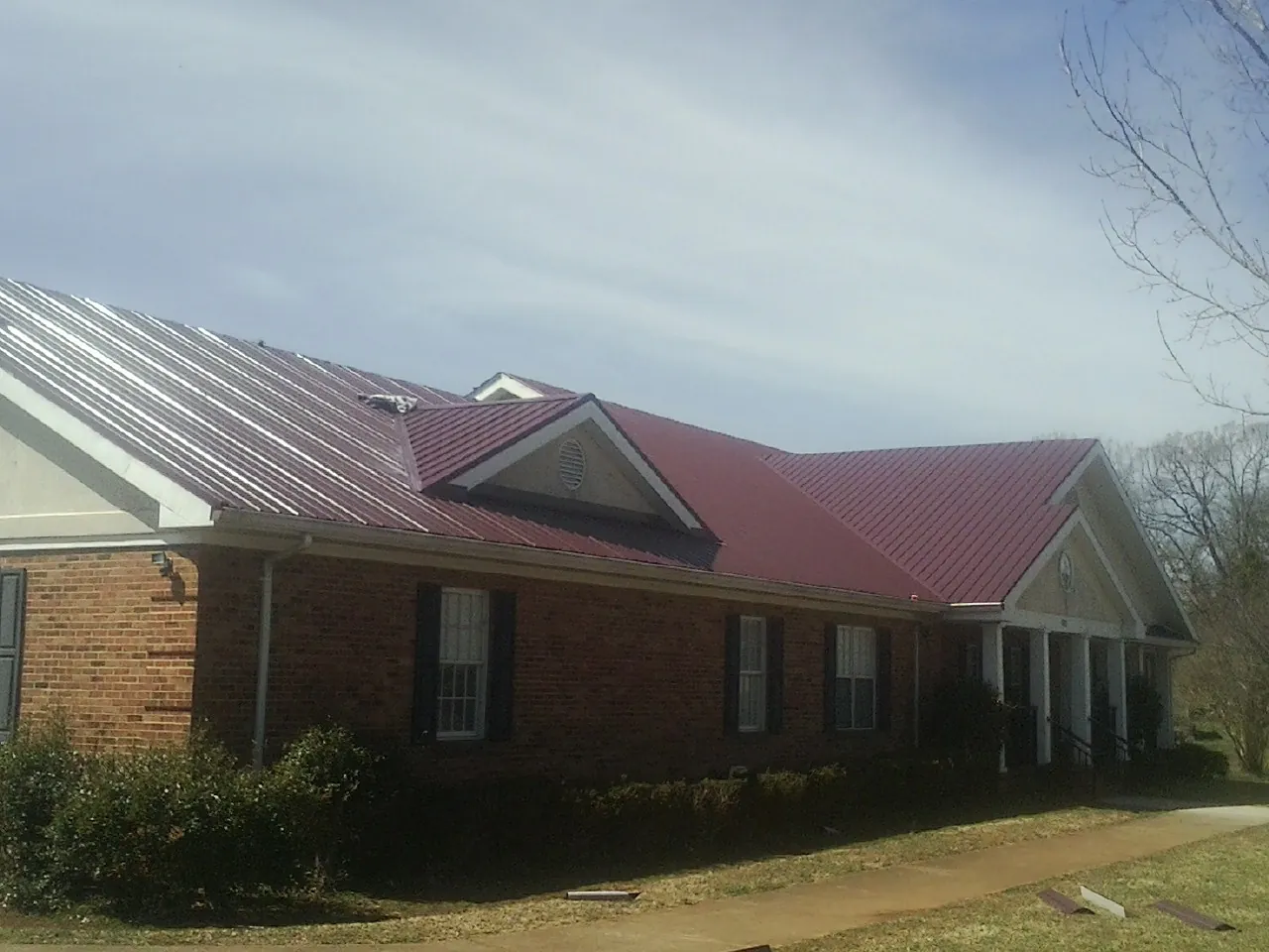 Red metal roof with gabled entries on a long brick building, from a Hail Damage Roof Repair job in Halbur