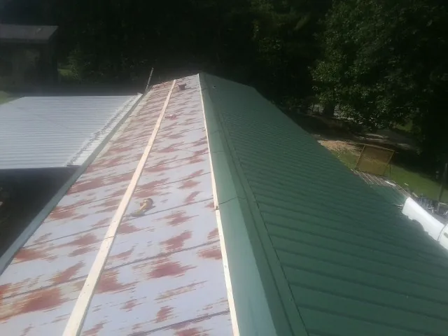 Old rusted panels beside newly installed green metal roofing — Wind Damage Roof Repair by Roofing Brothers in Halbur