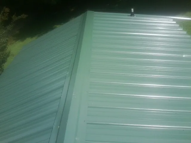 New green metal panels meeting at the ridge of a roof — Flat Roof Repair work by our crew in Halbur