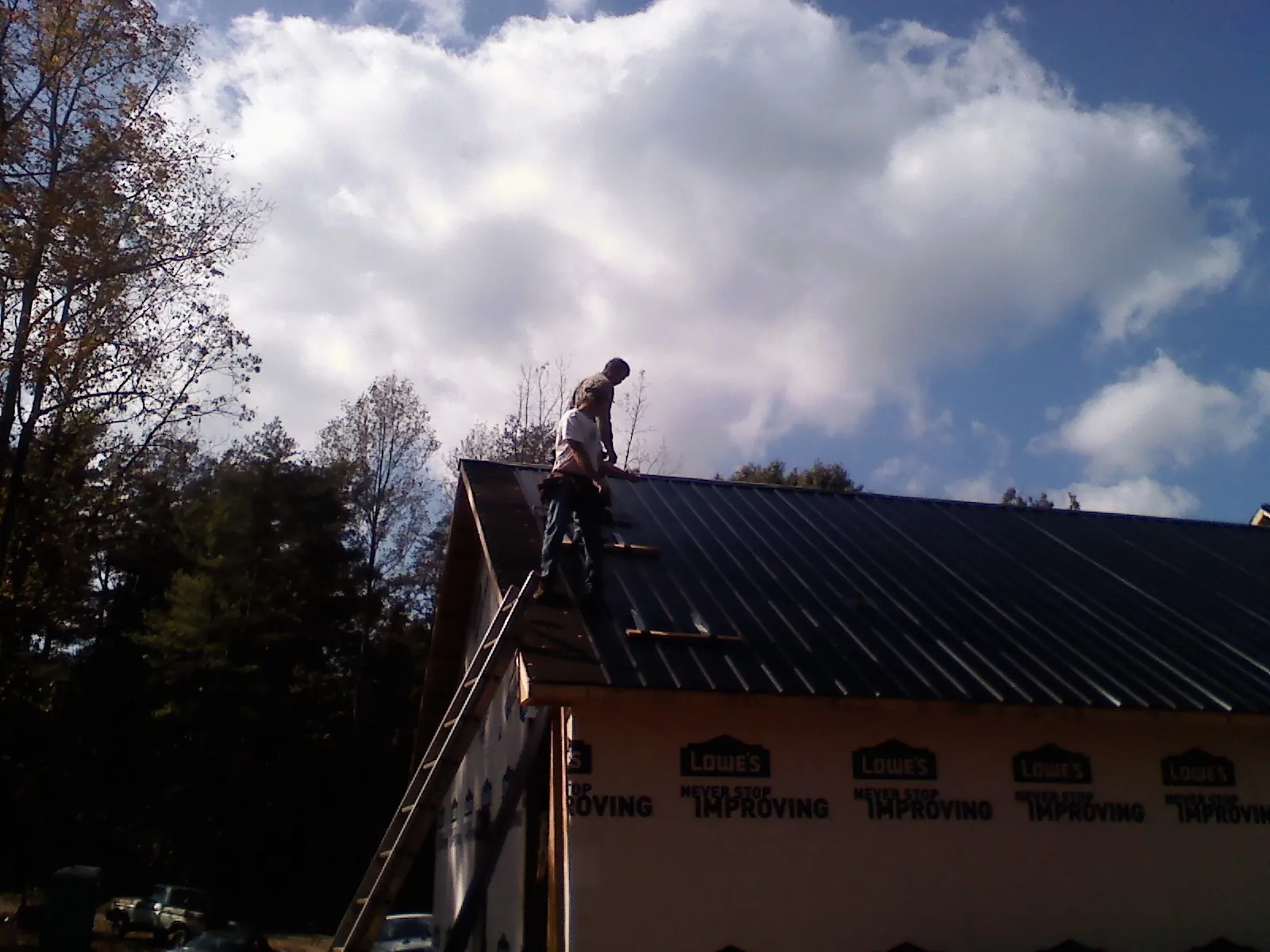 Roofer fastening dark metal panels high against a cloudy sky, from a Roof Inspection job in Halbur
